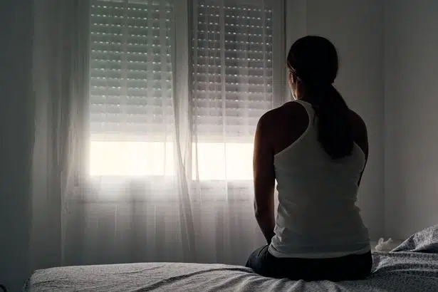0 rear view of an unrecognizable abused woman sitting on her bed looking out the window • mundo sombrio